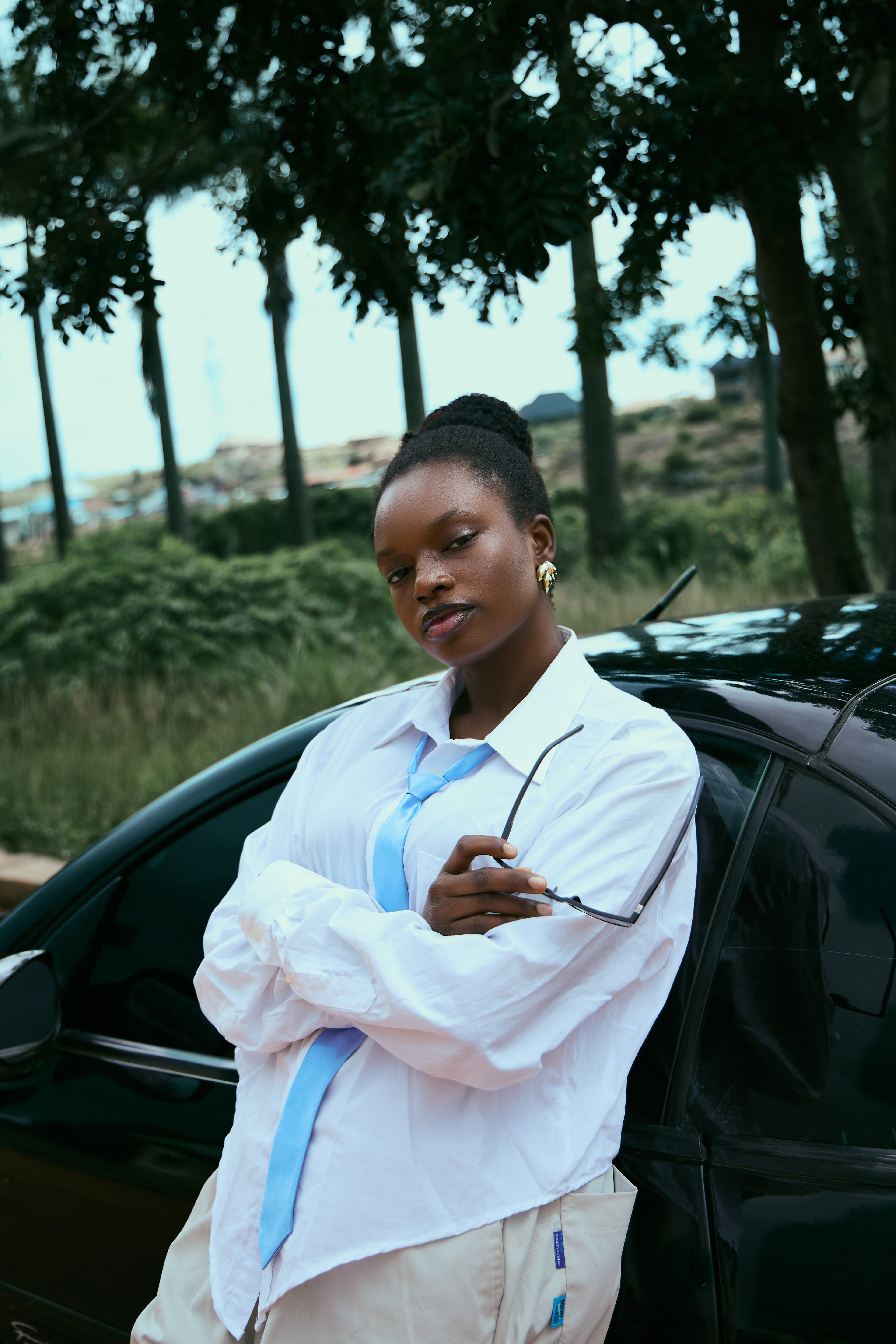 Jeyi in a white shirt and light-blue tie, leaning on a car